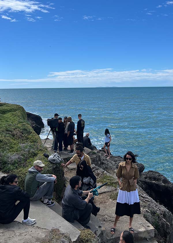 Behind the scenes of a fashion campaign shoot on the rocky cliffs of Monte Argentario, showing crew and equipment setup